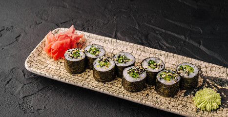 Delicious cucumber maki sushi sit on ceramic serving plate. Fresh Japanese food features spicy wasabi and pickled ginger. © AntAlexStudio