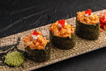 Three delicious gunkan maki feature spicy seafood tartar filling. Gourmet Japanese food sits on decorated plate with wasabi. © AntAlexStudio