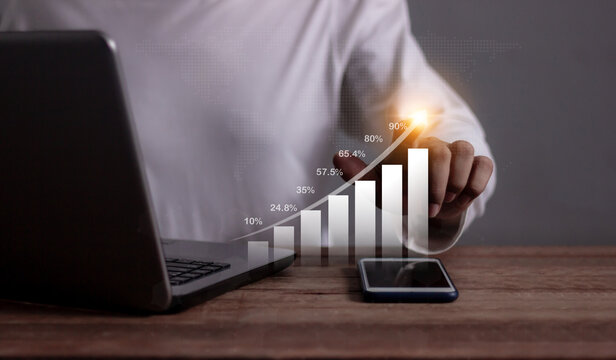 Young man with computer notebook and smartphone hand touching to visualize money growth The phone screen displays graphs and charts showing increasing investment and savings trends, increased account