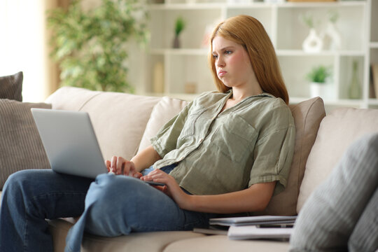 Overwhelmed blonde student checking laptop on a couch at home
