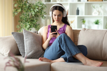 Obraz premium Serious teenage girl wearing headphone checking phone