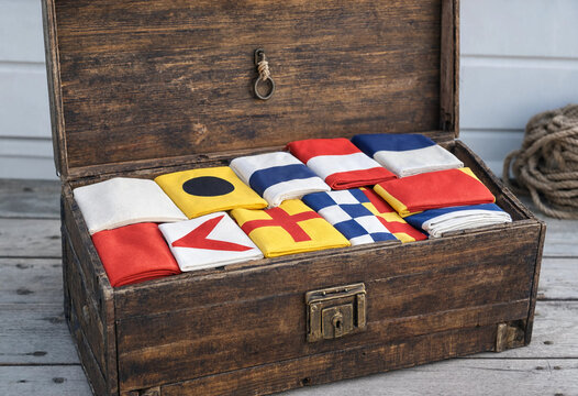 Antique wooden trunk filled with colorful nautical signal flags for maritime communication on a weathered wooden deck near the seaside shore