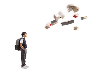 Obraz premium Surprised schoolboy standing and watching at flying books