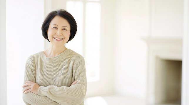 Lifestyle portrait of vibrant beautiful Japanese woman in her 50s, confident smiling pose with crossed hands, elegant casual outfit, bright airy white room, natural and studio soft lighting, clean col