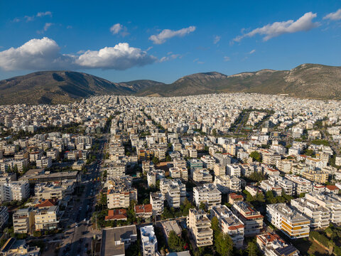 Aerial view of dense urban residential blocks with white buildings and rooftops under a blue sky with mountains in the background in Glyfada, Athens, Greece.