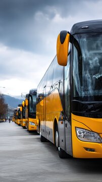 Row of modern yellow and black coaches parked in an outdoor lot on a cloudy day with mountain views in the distance and reflective windows shining brightly