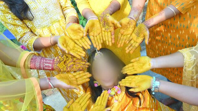 Close-up footage of a traditional Indian Haldi ceremony where family members and friends apply turmeric paste to the bride before marriage. The pre-wedding ritual symbolizes purification, blessings.