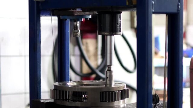 A close up vertical view of a hydraulic press piston rod pushing a metal spindle pin to disassemble a heavy duty planetary gear mechanism.