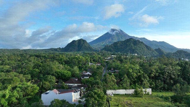 Aerial view of Mount Merapi volcano rising above the lush tropical forest and residential houses of Kaliurang in Pakem, Special Region of Yogyakarta, Indonesia.