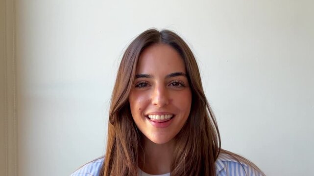 Front view of an attractive young woman smiling and talking during an online video call for work, remotely communicating with colleagues from her home office with a white background