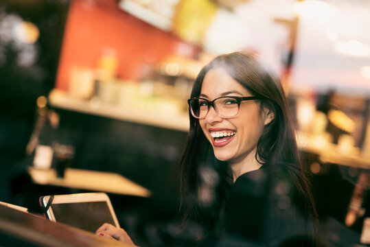 Pretty, brunette woman has a coffee in a bar while she looks at her tablet through the window
