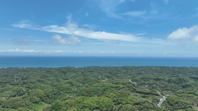Aerial view of lush green tropical hills and dense forest stretching towards the blue ocean horizon in Gunungkidul Regency, Special Region of Yogyakarta, Indonesia.