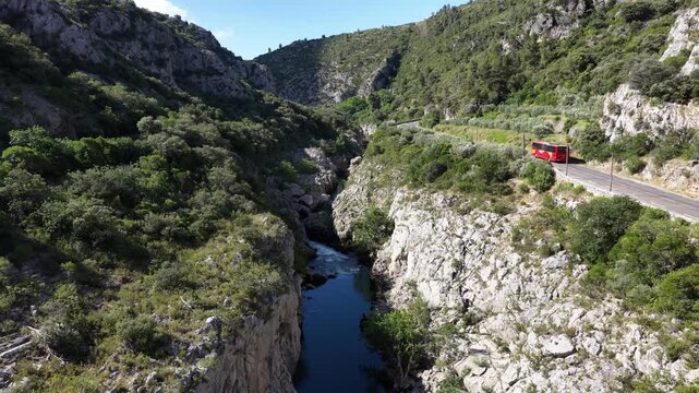 Aerial view of a deep green gorge with a winding river and road carved into the cliffs in southern France.