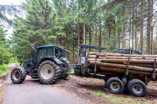 Pec pod Snezkou, Czech Republic - June 02, 2026: Valtra forestry tractor towing a Farma logging trailer loaded with timber logs on a mountain road.