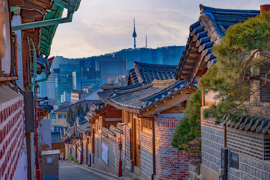 Beautiful contrast of traditional Bukchon Hanok Village streets with the modern city skyline and N Seoul Tower in the background during golden evening light, Seoul, South Korea.
