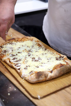 chef acabando de echar los ingredientes a una pizza artesanal rectangular de queso y carne