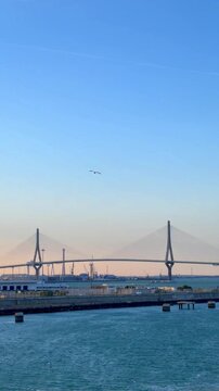 Beautiful coastal scenery of the constitution of 1812 bridge, also known as la pepa bridge, spanning the bay of cadiz with seagulls gracefully flying over the tranquil blue water at sunset