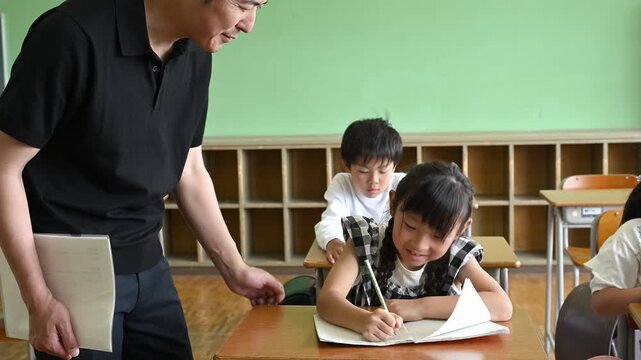教室で勉強する女子小学生を笑顔で優しく見守る男性教師