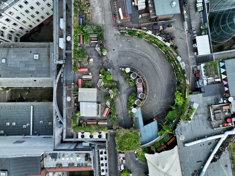 Aerial view of Klunkerkranich rooftop garden featuring lush greenery, wooden seating areas, and a circular ramp surrounded by urban architecture in Berlin, Berlin, Germany.