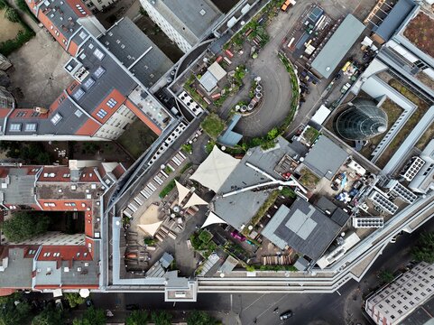 Aerial view of Klunkerkranich rooftop garden with people at outdoor seating and sunshades among the rooftops of Berlin, Berlin, Germany.