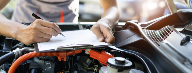 Obraz premium Auto check up and car service shop concept. Mechanic writing job checklist to clipboard to estimate repair quotation to client at workshop garage.