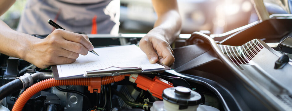Auto check up and car service shop concept. Mechanic writing job checklist to clipboard to estimate repair quotation to client at workshop garage.