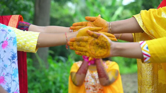 Close-up footage of a traditional Indian Haldi ceremony where family members and friends apply turmeric paste to the bride before marriage. The pre-wedding ritual symbolizes purification, blessings.