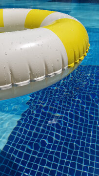 Summer vacation, summertime, leisure time, travel, tourism concept. Yellow and white striped inflatable swim ring floating in a bright blue tiled swimming pool. 