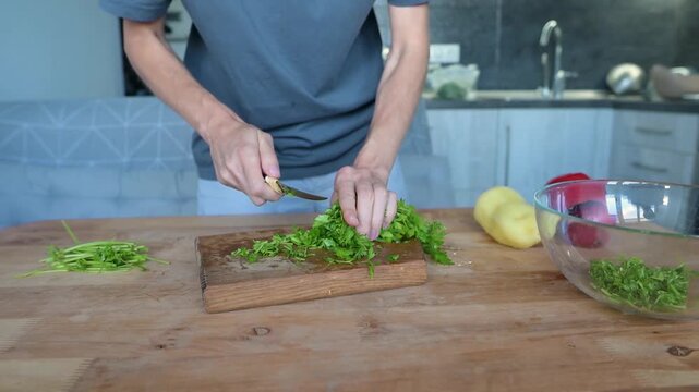 Person trimming fresh parsley stems on wooden cutting board in modern video Full HD kitchen