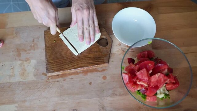 Person slicing tofu on wooden cutting board beside fresh vegetable salad in home kitchen video Full HD