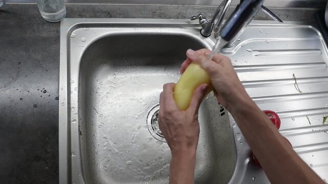 Washing yellow sweet pepper under running water in kitchen sink video Full HD