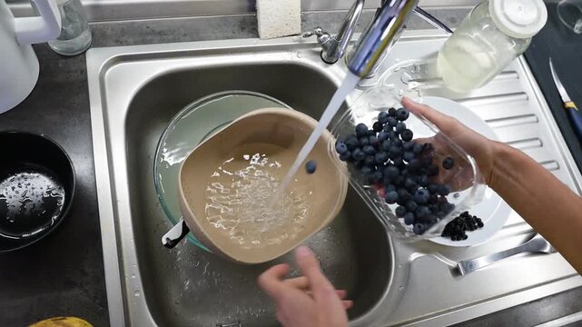 Pouring blueberries into colander and rinsing berries under kitchen faucet video Full HD