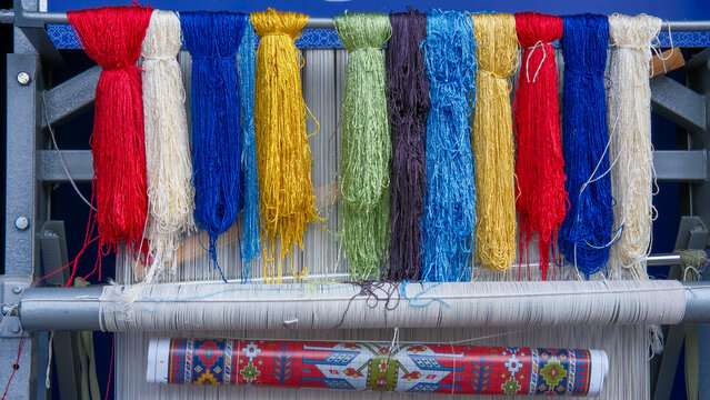 Yarn bundles, colorful skeins of silk or wool thread on metal bar of rug-weaving loom with talim. Carpet weaving craft, workshops and festivals. Creating traditional oriental intricate rugs