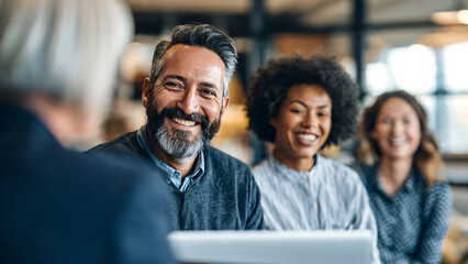Obraz premium Diverse male and female colleagues engaged in a productive discussion during a casual office meeting, professionals using a laptop and tablet to review ideas, share insights. 