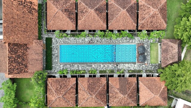 Aerial view of a rectangular blue swimming pool surrounded by stone paving and traditional terracotta-roofed villas in Borobudur, Central Java, Indonesia.