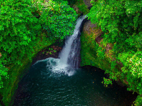 Aerial view of Wisata alam palak Siring kemumu waterfall cascading into a deep pool surrounded by lush tropical rainforest in Kecamatan Arma Jaya, Bengkulu, Indonesia.