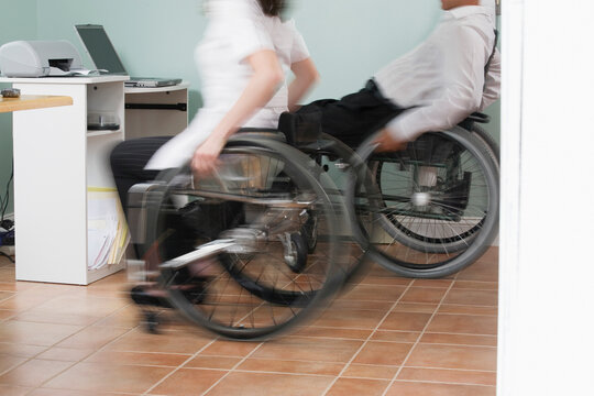 Man and a woman sitting in wheelchairs with a Spinal Cord Injury in a home office