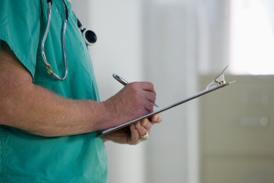 Mid section of doctor writing in clipboard