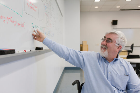 University professor with Muscular Dystrophy writing on a whiteboard in a classroom