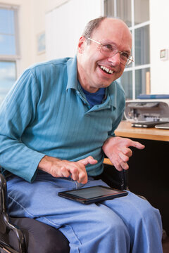 Man with Friedreich's Ataxia in wheelchair using a tablet with deformed hands