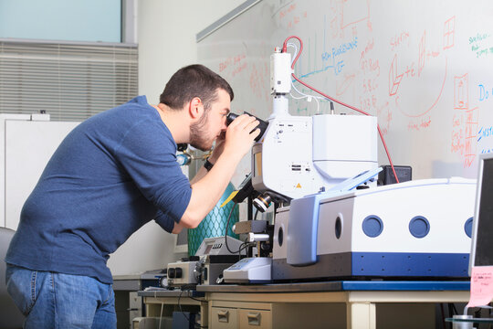 Engineering student looking through optical microscope on chemical analysis equipment in a
