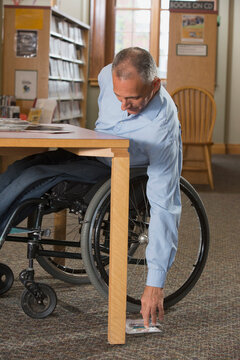 Man in a wheelchair with a Spinal Cord Injury in a library reaching for DVDs