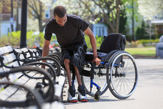 Man who had Spinal Meningitis getting out of a park bench and into his wheelchair