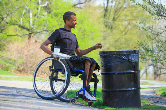 Man in a wheelchair who had Spinal Meningitis throwing away trash in a park