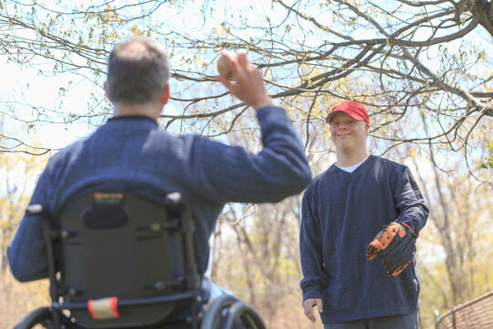 Father with Spinal Cord Injury and his son with Down Syndrome playing baseball in a park
