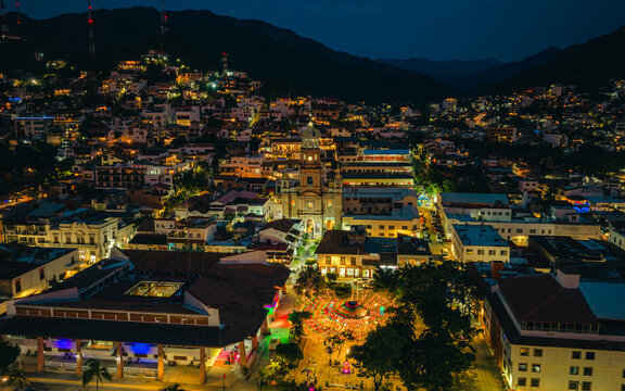 Aerial view of the Parish of Our Lady of Guadalupe and the illuminated city center at night with mountains in the background in Puerto Vallarta, Jalisco, Mexico.