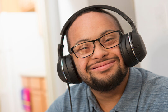 Happy African American man with Down Syndrome listening to music with headphones at home