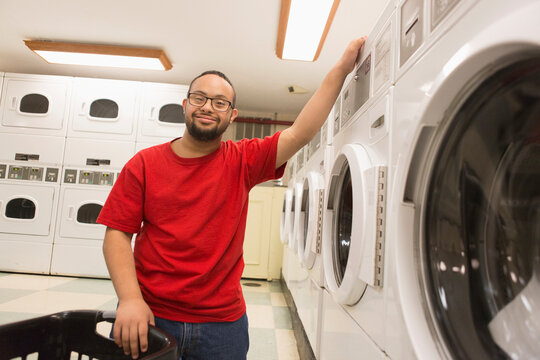 Happy African American man with Down Syndrome doing laundry in utility room