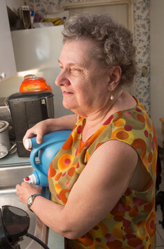 Blind senior woman pouring liquid into her sink in kitchen