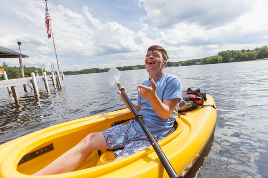 Happy young man with Down Syndrome rowing a kayak in a lake
